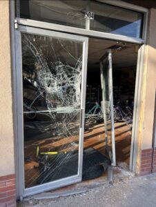 Handyman - before photo of door replacement and broken glass in a commercial storefront with cop car in the background